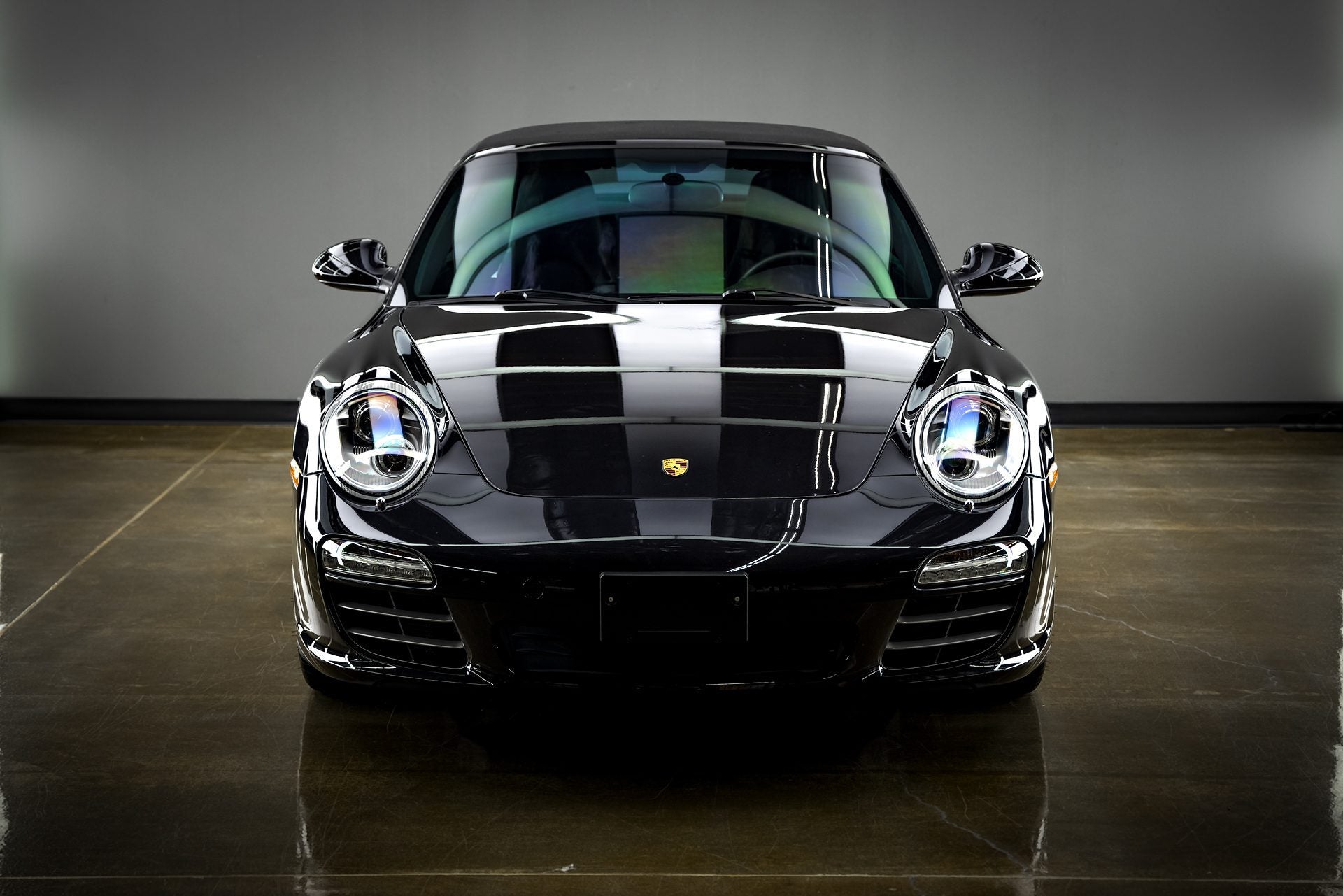 A front view of a deep black Porsche 911 Carrera, likely a model from the 997 generation (potentially a 2009-2012 model), showcasing the enhanced gloss and depth of color achieved through a professional ceramic coating application in Sydney, Chipping Norton, Western Sydney. The mirror-like finish highlights the protective benefits of a ceramic coating service available near you. Consider a ceramic coating near me to preserve the stunning appearance of your Porsche 911.