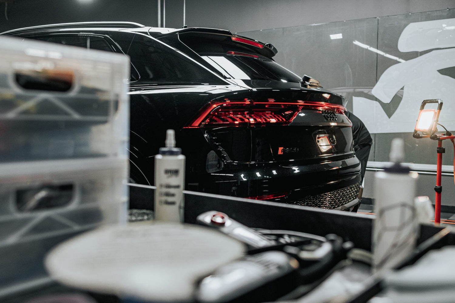 The rear of a sleek black Audi RS Q8 receiving professional car detailing in Sydney, New South Wales, Australia. The image shows the vehicle in a detailing studio, with various detailing products and tools in the foreground, emphasizing the comprehensive nature of car detailing near me. The glossy finish of the Audi highlights the quality of expert detailing services available. If you're looking for top-tier detailing near me to enhance and protect your luxury SUV, this Audi RS Q8 exemplifies the potential