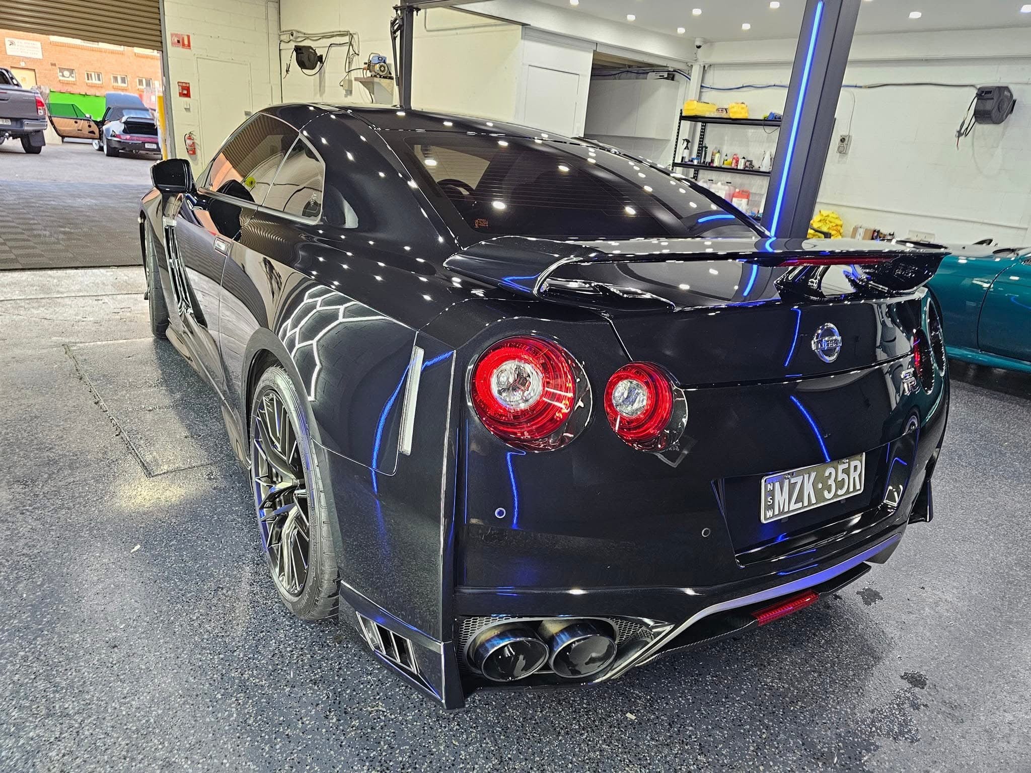 The rear view of a highly polished black Nissan GT-R, showcasing the deep, reflective shine achieved through a professional ceramic coating application at our detailing center in Western Sydney, Chipping Norton. The glossy finish and visible water beading highlight the protective properties of a quality ceramic coating service available near you in Western Sydney. If you're looking for premium ceramic coating near me in Chipping Norton