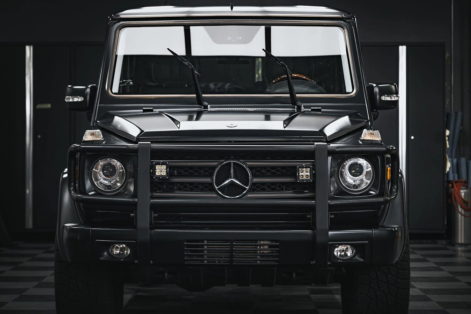 The imposing front view of a meticulously detailed black Mercedes-Benz G-Class, showcasing the results of professional paint correction and ceramic coating near me in Sydney, New South Wales, Australia. The deep, flawless shine of the paint, achieved through expert paint correction, is further enhanced and protected by a ceramic coating available near you. This image exemplifies the potential for a mirror-like finish and long-lasting durability offered by combining paint correction with ceramic coating.